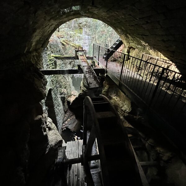 Seyon: Wasserrad in dunkler Schlucht mit Steg und Felswänden.