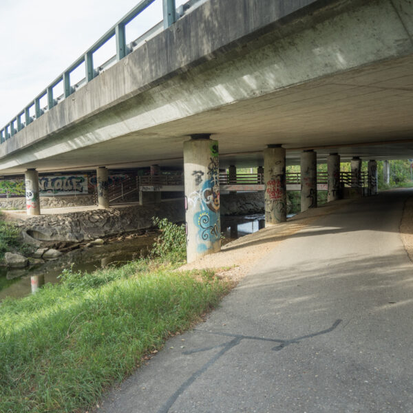 Betonbrücke über Sissle mit Graffiti-Kunst an den Säulen und einem Fußweg darunter.
