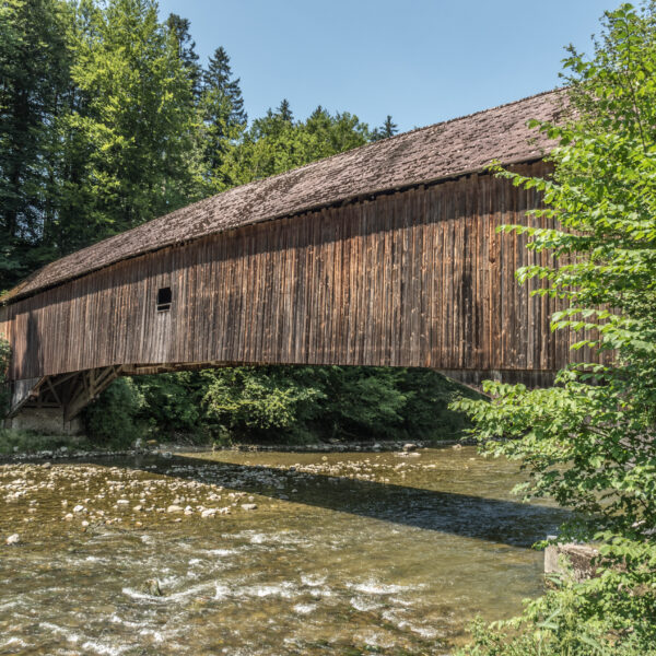 Gedeckte Holzbrücke über den Fluss Sitter, umgeben von Bäumen.