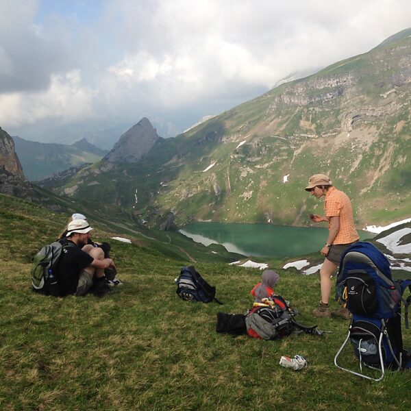 Wanderer rasten am Spilauersee in den Schweizer Alpen. Grüne Wiesen und Berglandschaft.
