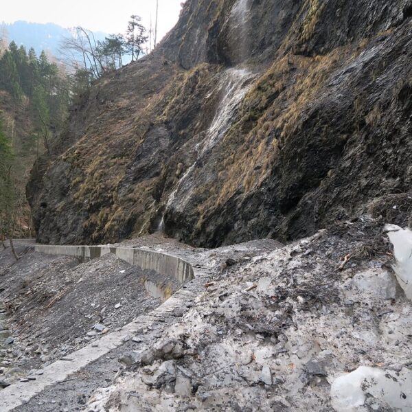 Tamina: Fluss neben einer Bergstraße mit Felswand und Geröllhalde. Schnee liegt am Weg.