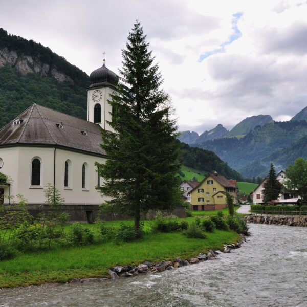 Kirche am Fluss in Thur, Schweiz, mit Bergen im Hintergrund. Ruhige Landschaft.