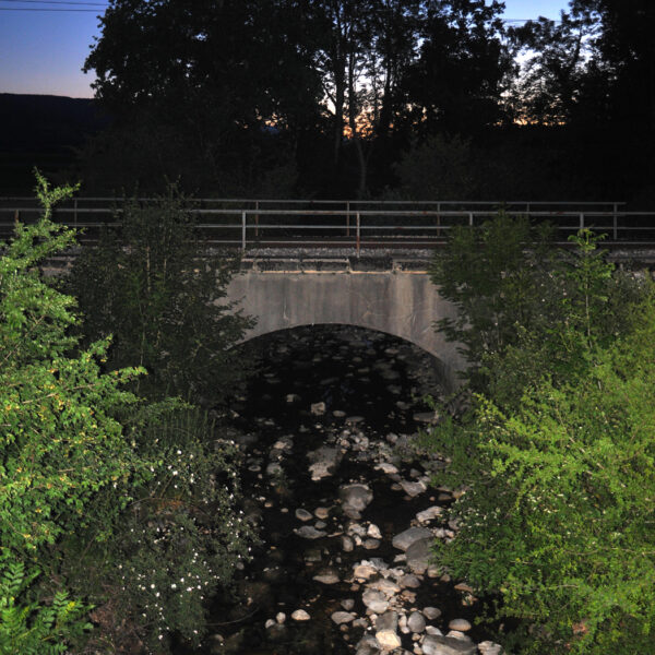 Steiniger Bach unter einer Eisenbahnbrücke bei Dämmerung. Veyron.