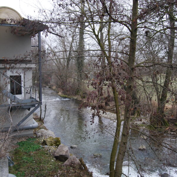 Fluss Wyna neben einem Gebäude mit Bäumen im Winter.